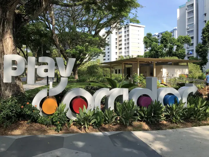 A dog walking on the perimeter loop of Bedok Town Park on Bedok North Avenue 3, Singapore, with mature rain trees overhead and a quiet HDB block visible through the trees.