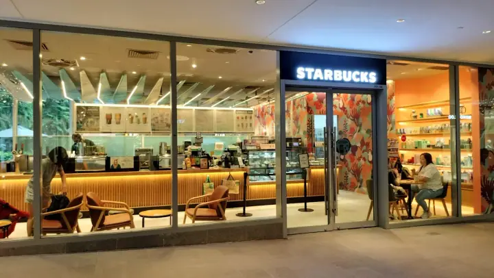 A dog standing with its owner inside One Holland Village mall, Singapore, with the open atrium, dog-friendly tenant signs, and the outdoor plaza visible through the windows.