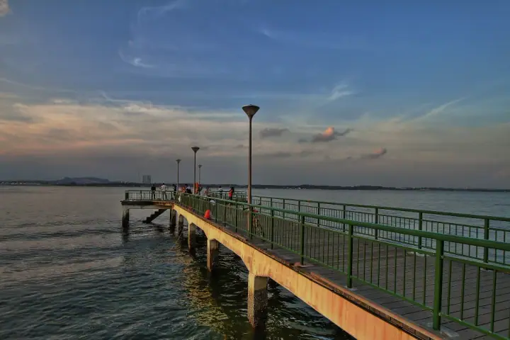A calm dog on the sand at Sembawang Park Beach in Sembawang, Singapore, with gentle waves and warm golden-hour light, a few paw-prints softly in the foreground.