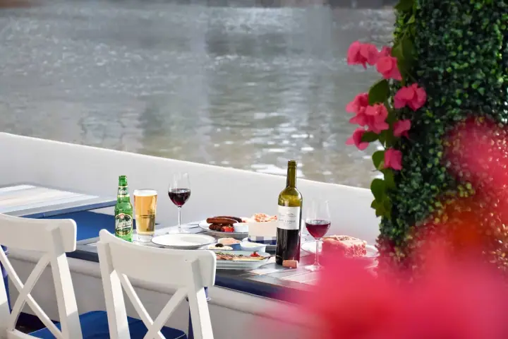 A medium-sized dog sitting beside its owner at the riverside outdoor terrace of Zorba The Greek Taverna at ORA Block A, Clarke Quay, Singapore, with the Singapore River and lit-up Robertson Quay buildings in the background.